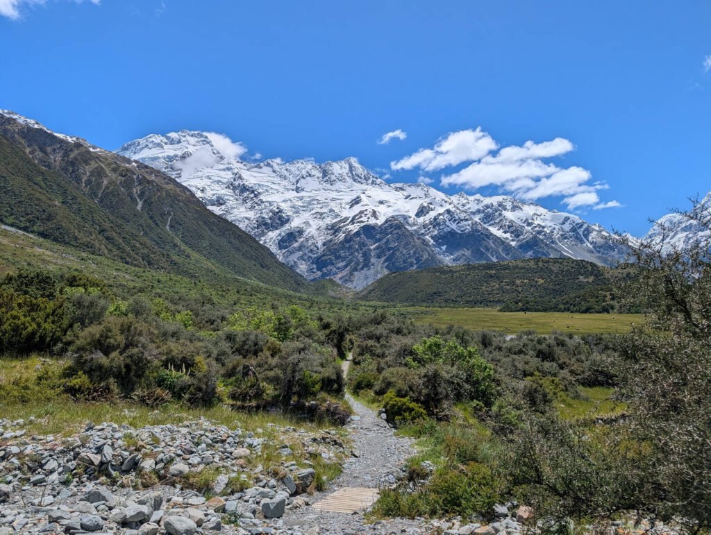 Snow-capped Mount Cook rising above a green valley with a walking trail in New Zealand’s South Island