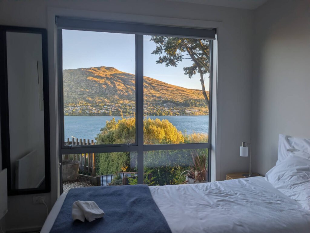 View of Lake Wakatipu and surrounding hills in Queenstown seen through a bedroom window in the early morning light
